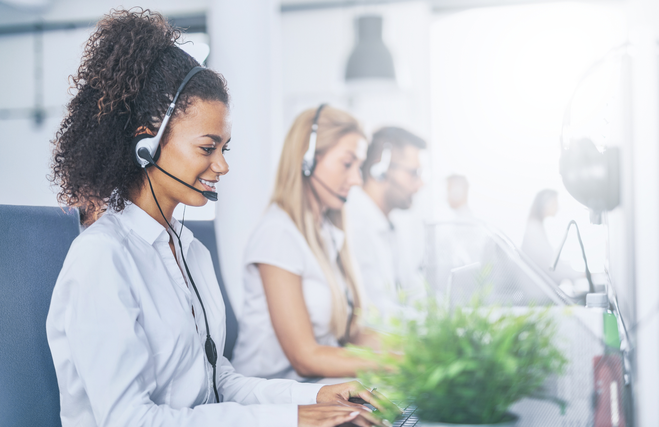 A group of proactive customer service reps seated at a desk, wearing headsets, and answering customer calls